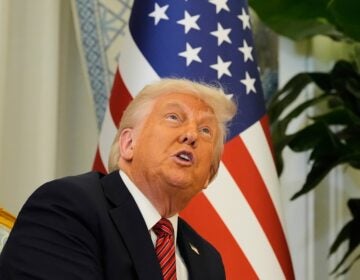 Donald Trump sits in front of an American flag